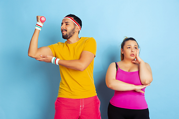 Image showing Young pretty caucasian couple in bright clothes training on blue background