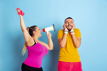 Image showing Young pretty caucasian couple in bright clothes training on blue background