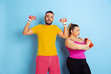 Image showing Young pretty caucasian couple in bright clothes training on blue background