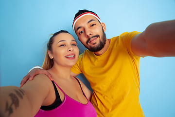 Image showing Young pretty caucasian couple in bright clothes training on blue background