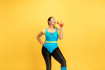 Image showing Young caucasian plus size female model\'s training on yellow background