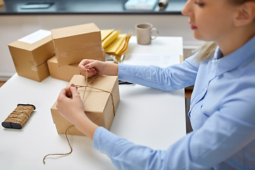 Image showing woman packing parcel and tying rope at post office