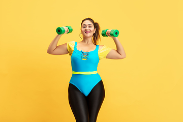 Image showing Young caucasian plus size female model\'s training on yellow background