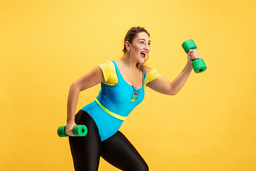 Image showing Young caucasian plus size female model\'s training on yellow background