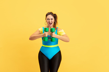 Image showing Young caucasian plus size female model\'s training on yellow background