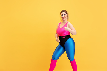 Image showing Young caucasian plus size female model\'s training on yellow background