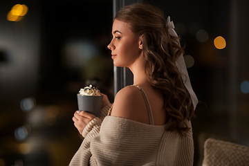 Image showing woman holding mug with whipped cream at night