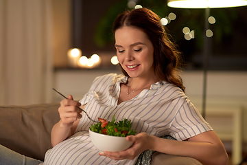 Image showing happy smiling pregnant woman eating salad at home