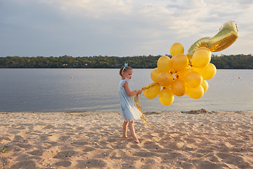 Image showing Little girl with many golden balloons on the beach at sunset