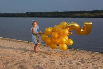 Image showing Little girl with many golden balloons on the beach at sunset