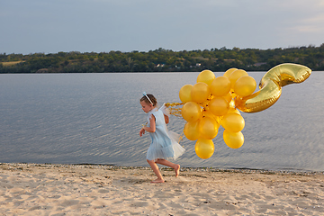 Image showing Little girl with many golden balloons on the beach at sunset