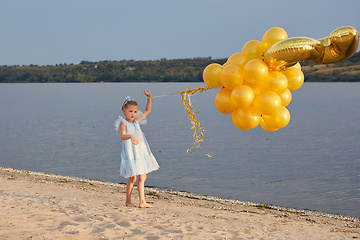 Image showing Little girl with many golden balloons on the beach at sunset