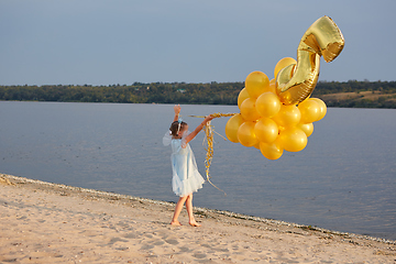 Image showing Little girl with many golden balloons on the beach at sunset