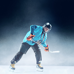 Image showing Young female hockey player with the stick on ice court and blue background