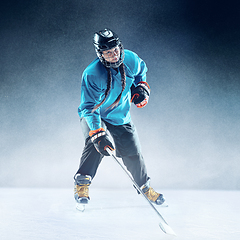 Image showing Young female hockey player with the stick on ice court and blue background