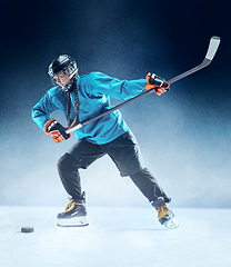 Image showing Young female hockey player with the stick on ice court and blue background