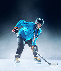 Image showing Young female hockey player with the stick on ice court and blue background