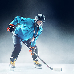 Image showing Young female hockey player with the stick on ice court and blue background