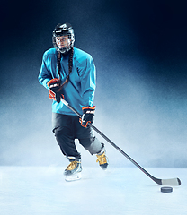 Image showing Young female hockey player with the stick on ice court and blue background