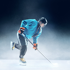 Image showing Young female hockey player with the stick on ice court and blue background