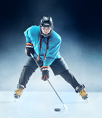 Image showing Young female hockey player with the stick on ice court and blue background