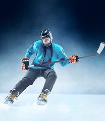 Image showing Young female hockey player with the stick on ice court and blue background