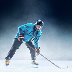 Image showing Young female hockey player with the stick on ice court and blue background