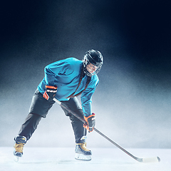 Image showing Young female hockey player with the stick on ice court and blue background