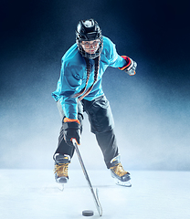 Image showing Young female hockey player with the stick on ice court and blue background