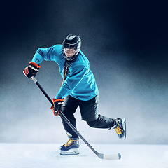 Image showing Young female hockey player with the stick on ice court and blue background