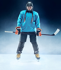 Image showing Young female hockey player with the stick on ice court and blue background