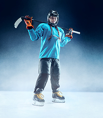 Image showing Young female hockey player with the stick on ice court and blue background