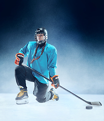Image showing Young female hockey player with the stick on ice court and blue background