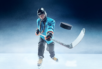 Image showing Young female hockey player with the stick on ice court and blue background