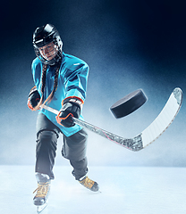 Image showing Young female hockey player with the stick on ice court and blue background