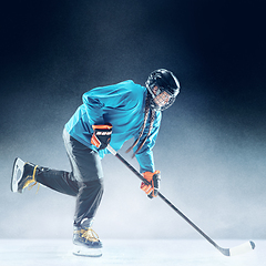 Image showing Young female hockey player with the stick on ice court and blue background