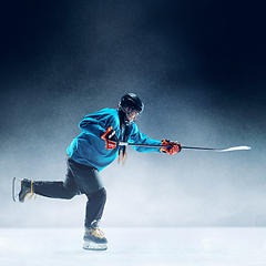 Image showing Young female hockey player with the stick on ice court and blue background