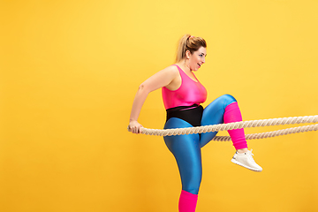 Image showing Young caucasian plus size female model\'s training on yellow background