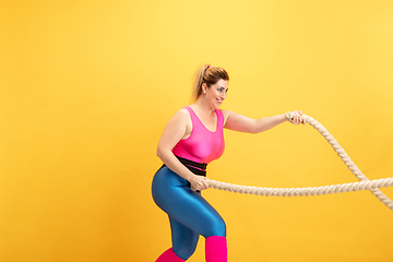 Image showing Young caucasian plus size female model\'s training on yellow background