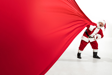 Image showing Santa Claus pulling huge bag full of christmas presents isolated on white background