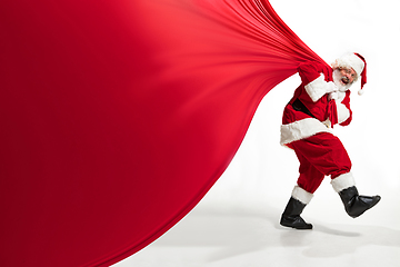 Image showing Santa Claus pulling huge bag full of christmas presents isolated on white background