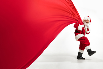 Image showing Santa Claus pulling huge bag full of christmas presents isolated on white background