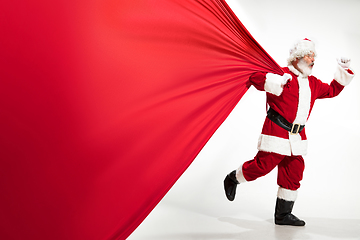 Image showing Santa Claus pulling huge bag full of christmas presents isolated on white background