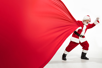 Image showing Santa Claus pulling huge bag full of christmas presents isolated on white background