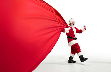 Image showing Santa Claus pulling huge bag full of christmas presents isolated on white background