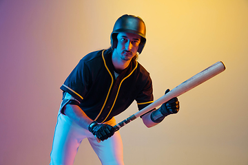 Image showing Baseball player, pitcher in a black uniform practicing on gradient background in neon light