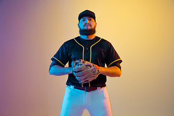 Image showing Baseball player, pitcher in a black uniform practicing on gradient background in neon light