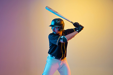 Image showing Baseball player, pitcher in a black uniform practicing on gradient background in neon light