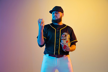 Image showing Baseball player, pitcher in a black uniform practicing on gradient background in neon light