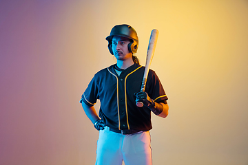 Image showing Baseball player, pitcher in a black uniform practicing on gradient background in neon light